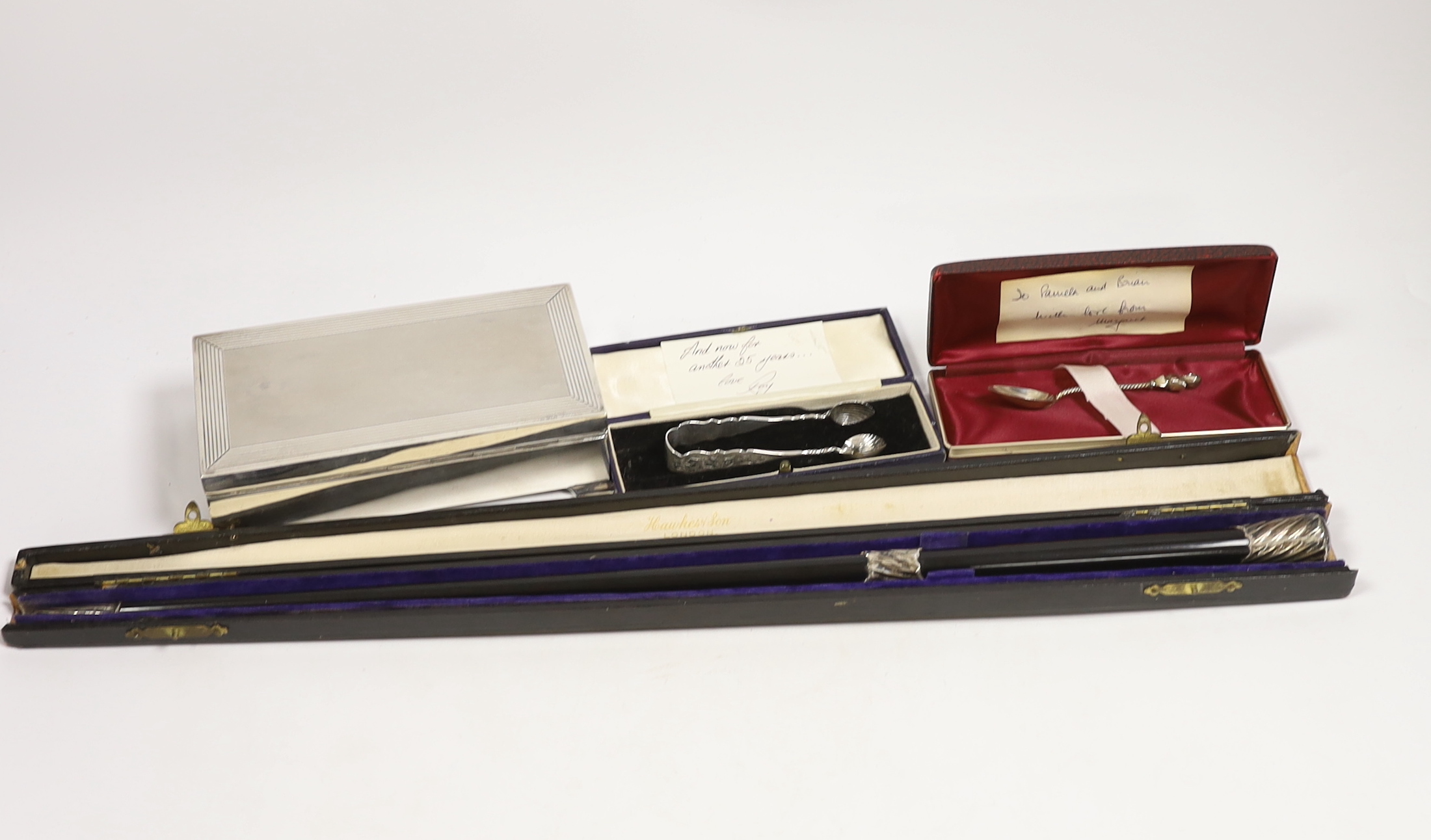 An Elizabeth II silver mounted rectangular cigarette box, Birmingham, 1963, 17.4cm, a cased 1920's silver mounted ebonised conductor's baton, 52.5cm, a pair of silver sugar tongs and a small silver spoon.